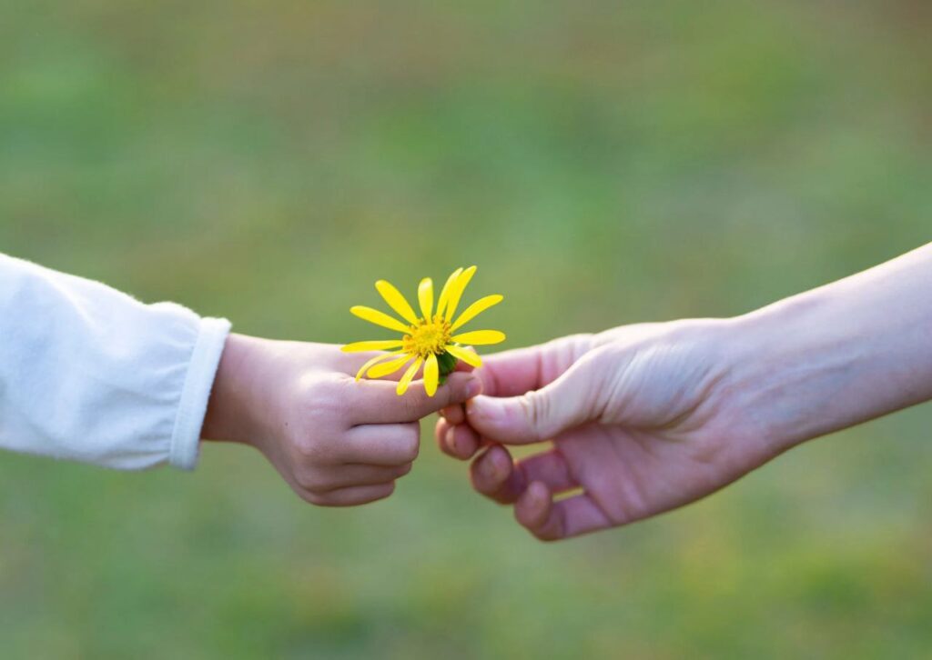 mano de un niño y mano de mama con una flor amarilla